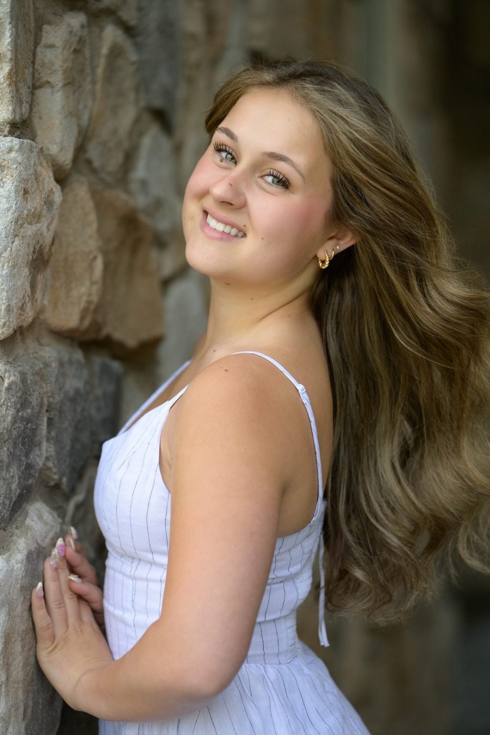 Graduate in a white dress photographed against a stone wall during her grad portrait session in Langley, BC