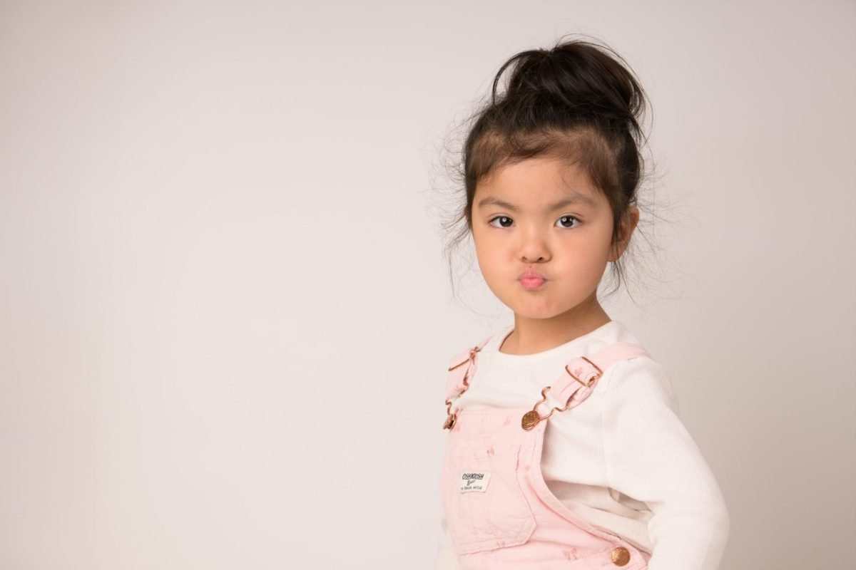 Preschool portrait of a girl in pink overalls pulling a playful face on photo day