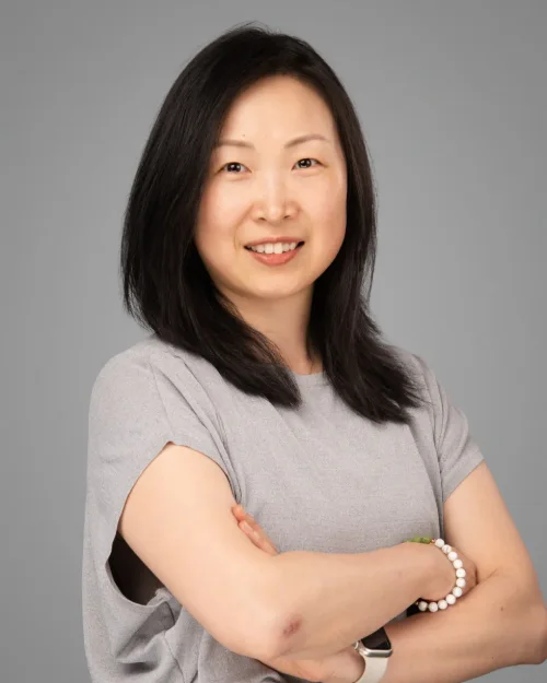 Conference headshot of a woman in a grey tee with arms crossed