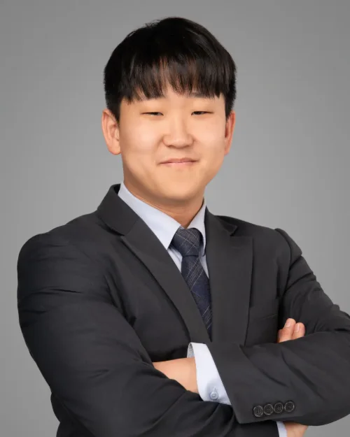 Conference headshot of a young man in a dark suit and tie, arms crossed