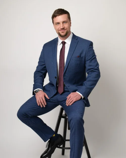 Full length personal branding portrait of a man in a blue suit seated on a stool