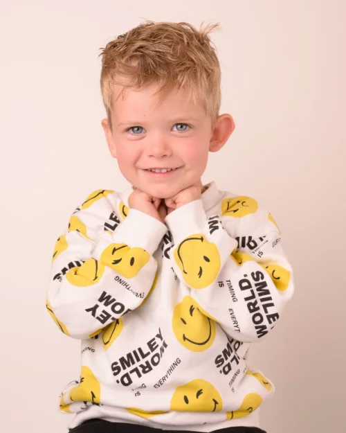 A boy in a smiley-face fleece top with his arms wrapped around himself
