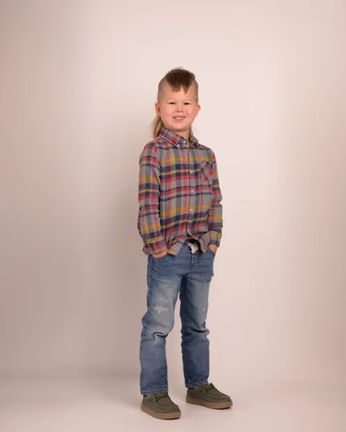 A boy in a plaid shirt and jeans photographed head to toe