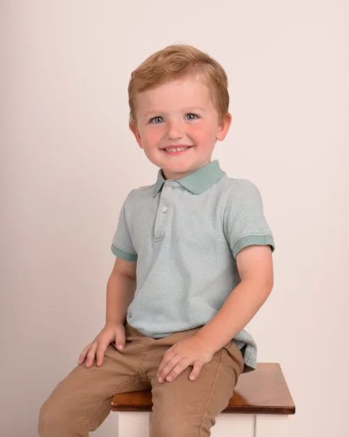 A boy in a mint polo sitting on a wooden stool