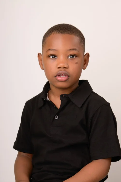 A boy in a black polo shirt on a warm neutral backdrop