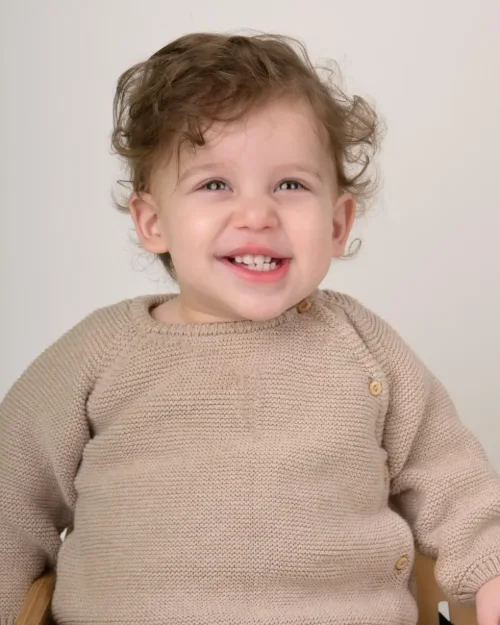 A curly-haired toddler boy in a cream knit sweater