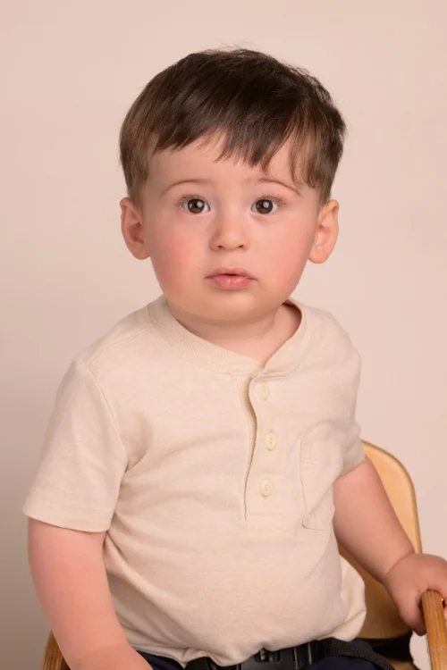 A toddler boy in a cream henley on a warm neutral backdrop