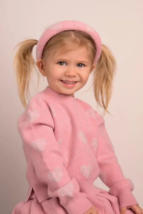 A girl with pigtails and a pink headband in a soft pink sweater