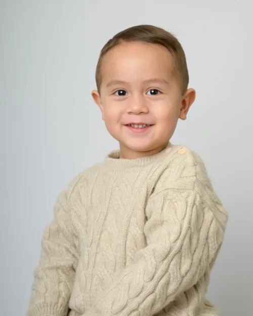 A boy in a cream cable-knit sweater smiling