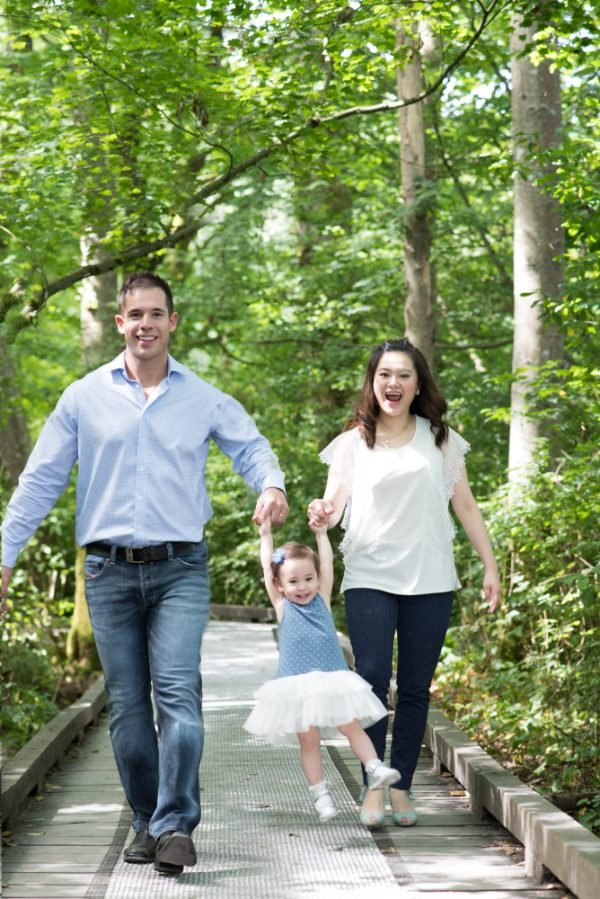 Parents swinging their daughter between them on a forest boardwalk in Langley