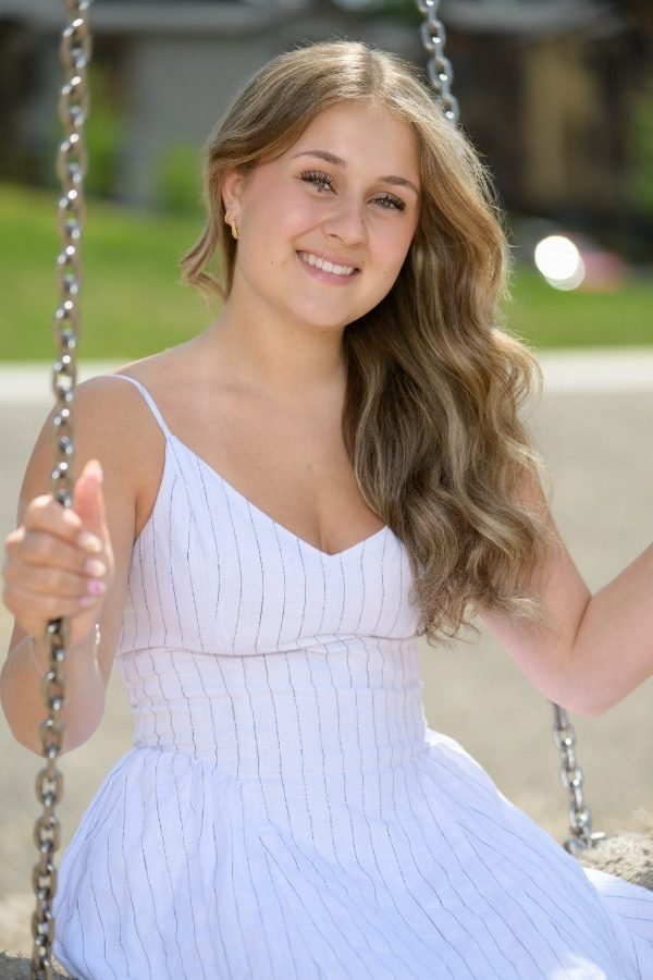 Graduate on a swing in a white dress during an outdoor grad session in Langley