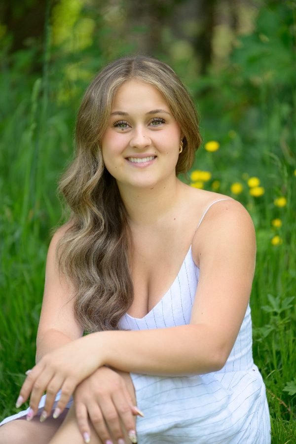 Graduate in a white summer dress seated in tall grass at a Fraser Valley grad session