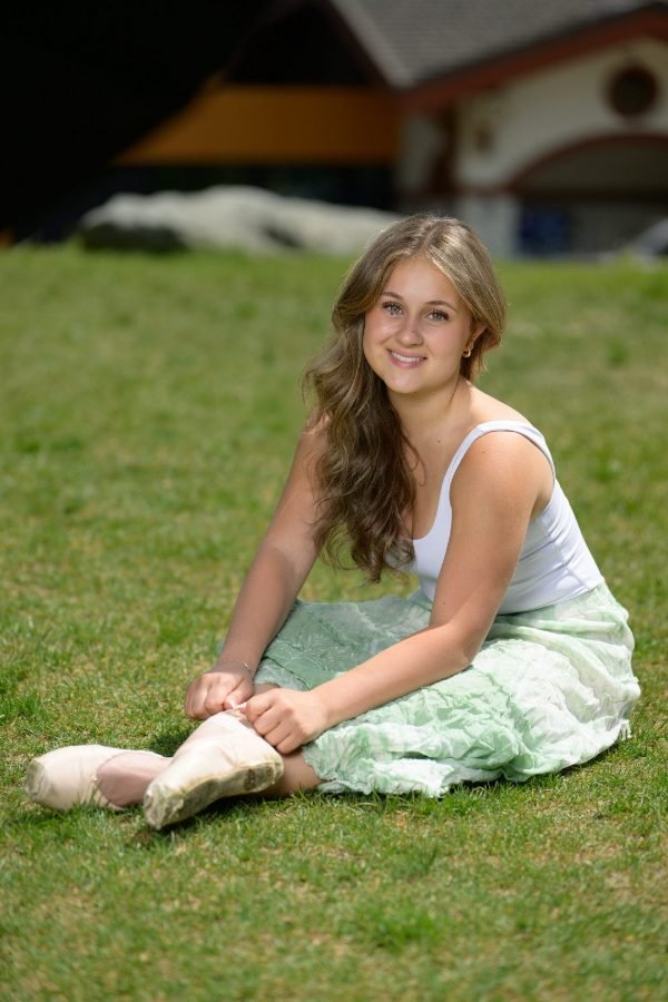 Graduating dancer tying her pointe shoes on the grass during a Langley grad session