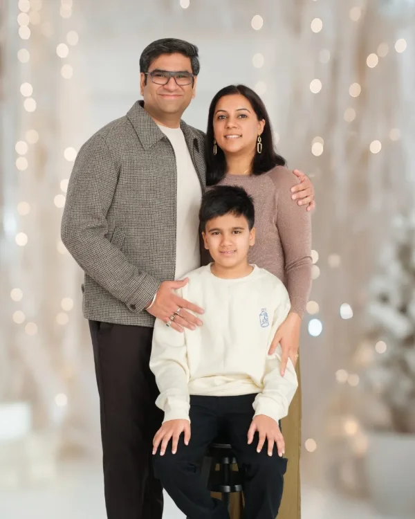 Parents standing with their son on a stool in front of warm holiday lights