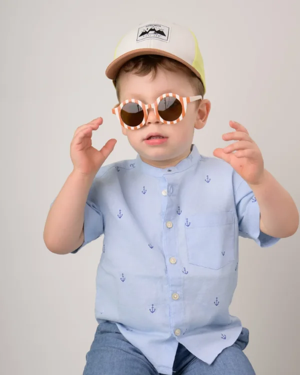 A toddler being silly in a ball cap and round play sunglasses on photo day