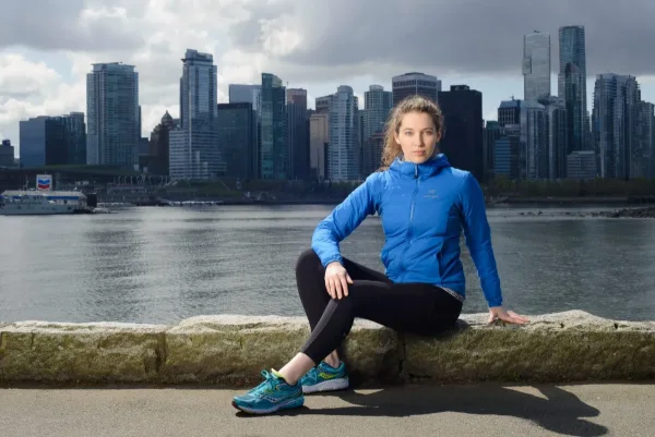 Activewear brand photography of a model seated on the seawall with the Vancouver skyline behind