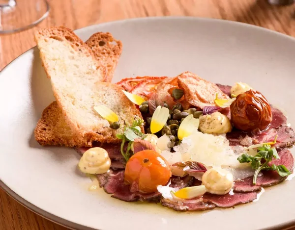 Menu photography of beef carpaccio with capers, parmesan and grilled bread on a ceramic plate
