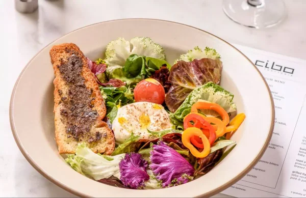 Restaurant food photography of a burrata and garden salad bowl plated beside a menu at a Vancouver trattoria