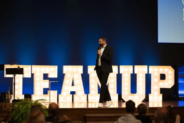 Host on stage beside illuminated marquee letters at a charity impact gala