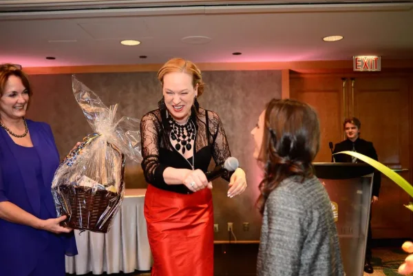 Host presenting a raffle prize basket to a winning guest during a charity gala
