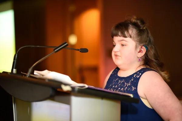 Young guest speaker sharing her story from the podium at a charity fundraising gala