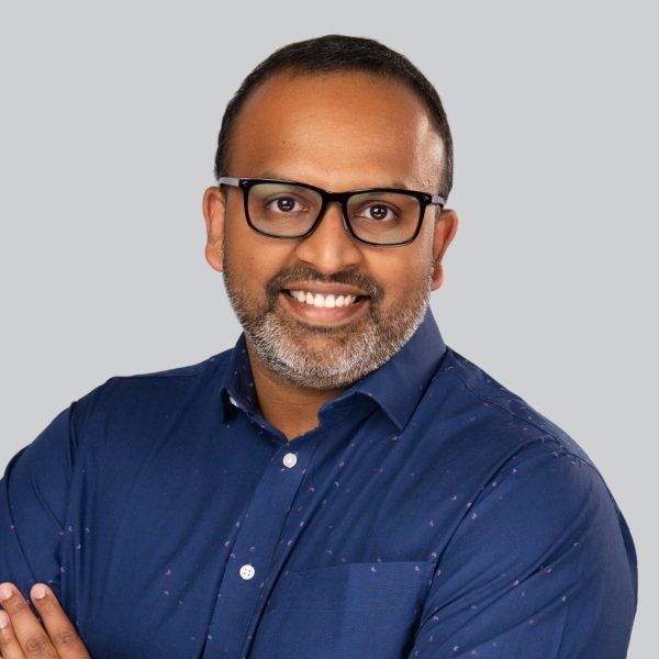 Conference headshot of a man in glasses and a blue denim shirt at an event booth