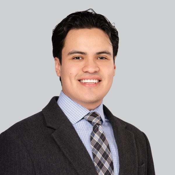Conference headshot of a man in a grey plaid blazer and patterned tie