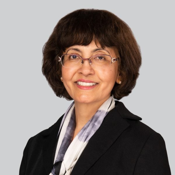Conference headshot of a woman in a dark blazer and printed scarf on a grey backdrop