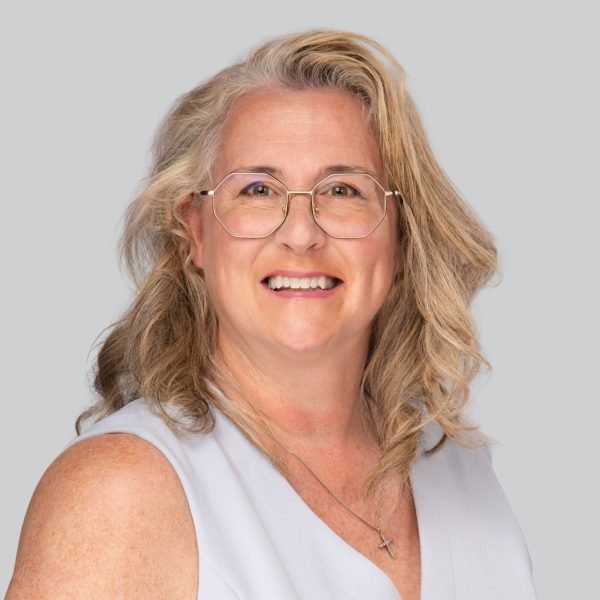 Event headshot of a woman with blonde curly hair and glasses on a grey backdrop
