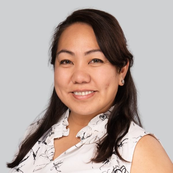 Event headshot of a woman in a white floral blouse on a grey backdrop