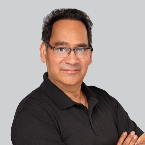 Trade show headshot of a man in glasses and a black polo shirt, arms crossed