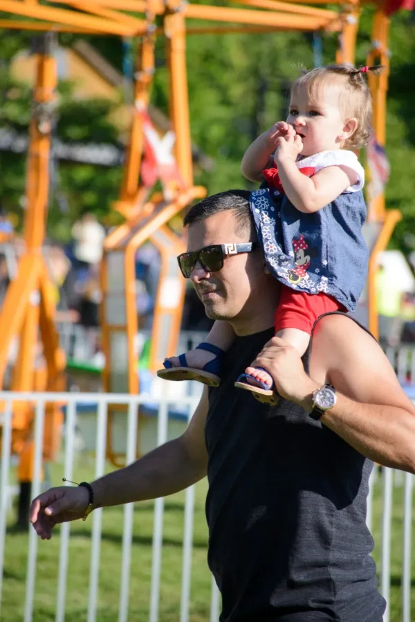 Father carrying his daughter on his shoulders through the crowd at a Canada Day celebration