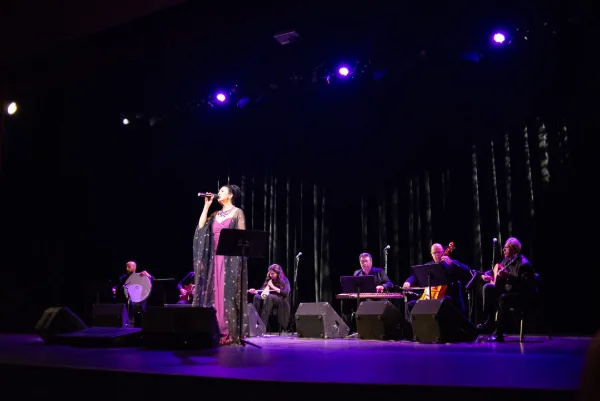 Vocalist and acoustic ensemble under deep blue stage lighting at a theatre concert in Vancouver