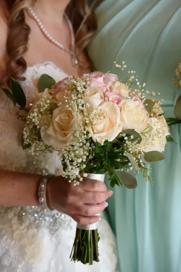 Close up of a bridal bouquet of cream and blush roses with baby’s breath held by the bride
