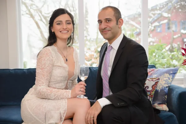 Newly married couple raising a glass indoors at their small winter wedding while snow falls outside the window