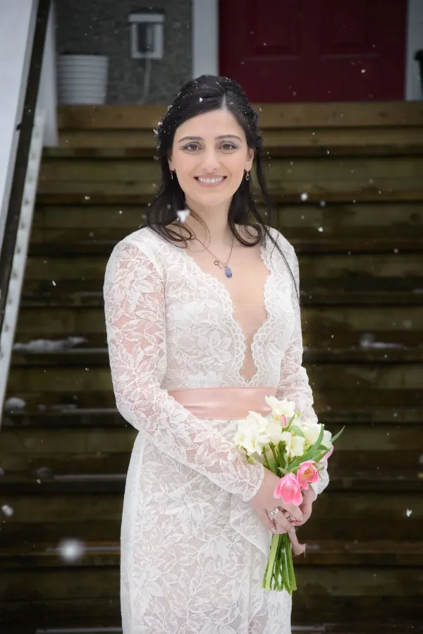 Winter bride portrait in a lace gown holding tulips as snow falls on the front steps