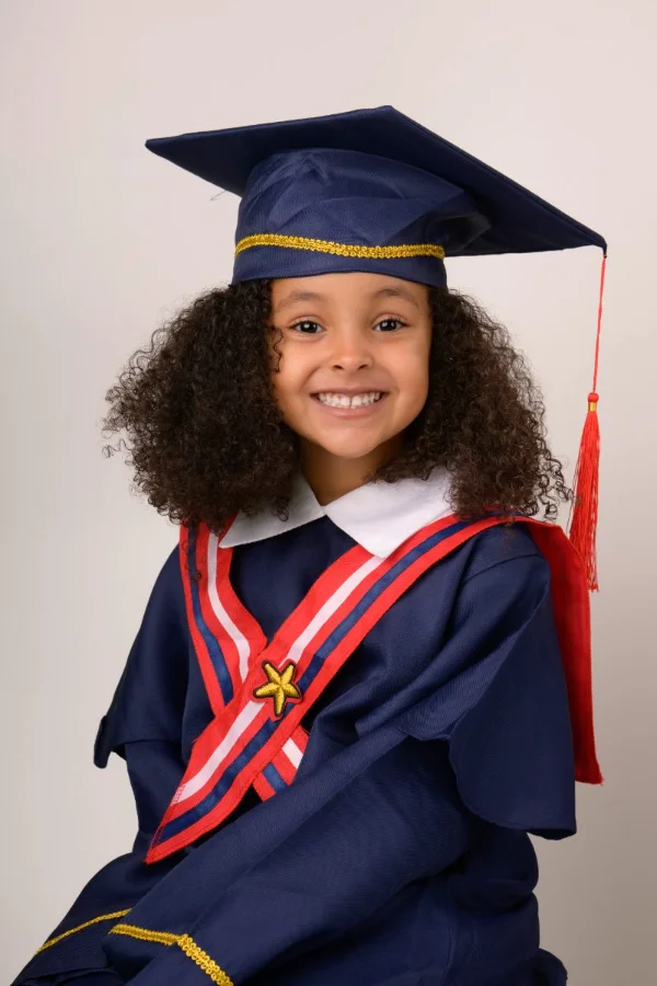 A preschool graduate with curly hair in a navy cap and gown