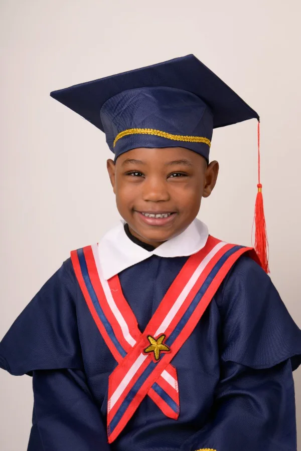 A preschool graduate in a navy cap and gown with a red and white stole