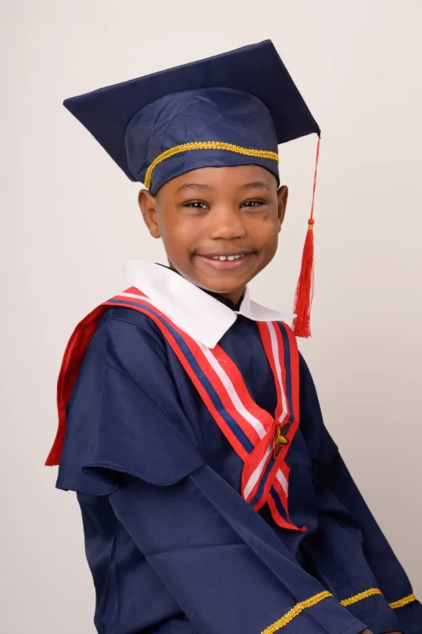 A preschool graduate in a navy cap and gown with a red and white stole
