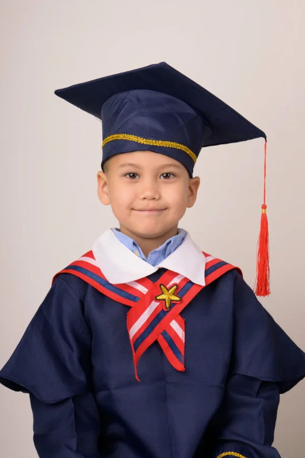 A preschool graduate in a navy cap and gown with his hands folded