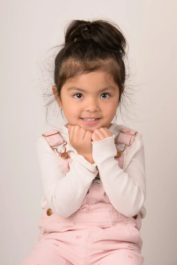 A girl with a top-knot resting her chin on her hands, warm neutral backdrop