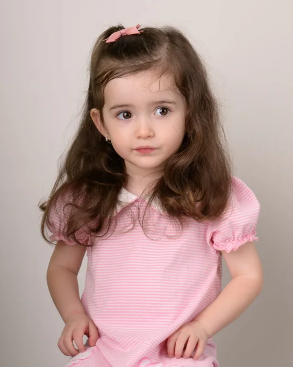 A girl in a pink striped top on a soft grey backdrop