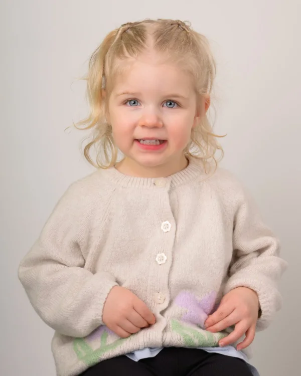 A toddler girl in a cream cardigan on a soft grey backdrop