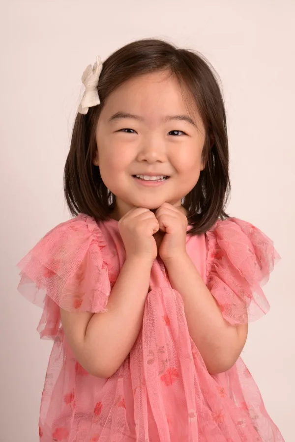 A girl in a pink ruffled top on a warm blush backdrop