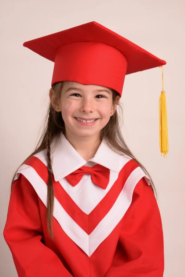 A preschool graduate in a red cap and gown with a white stole