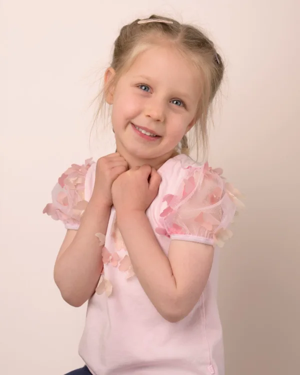 A girl in a pale pink puff-sleeve top with her hands clasped