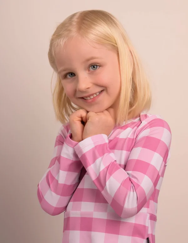A girl in a pink gingham top on a soft grey backdrop