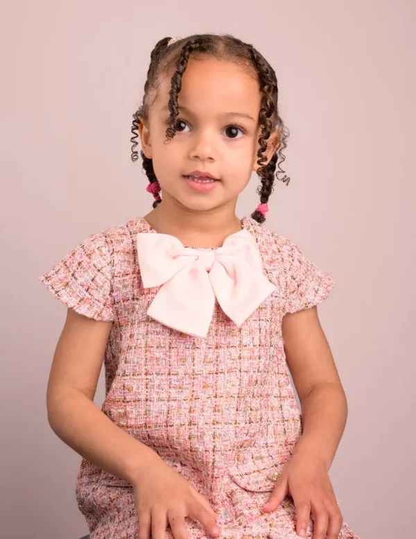 A preschool girl in a pink floral dress with a bow, hands together