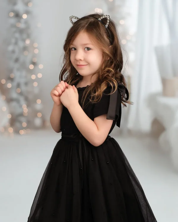 A preschool girl in a black tulle dress and sparkly headband in a bright studio set