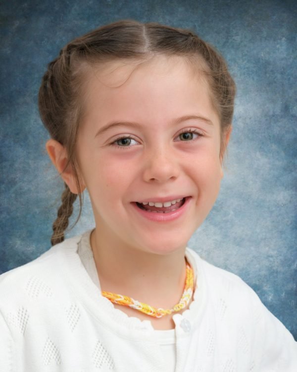 A student in a white cardigan photographed on the classic blue school-photo backdrop